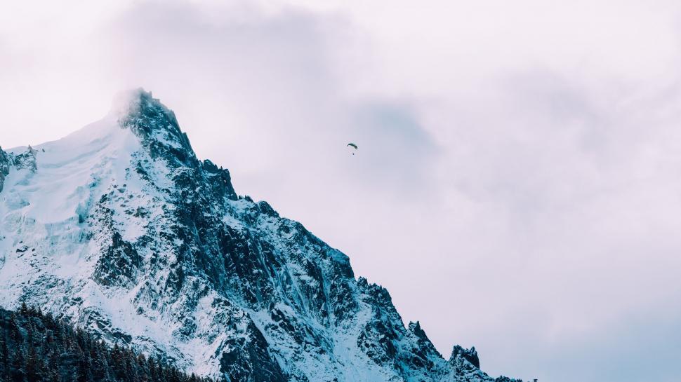 Free Image of A person flying in the sky over a snowy mountain 