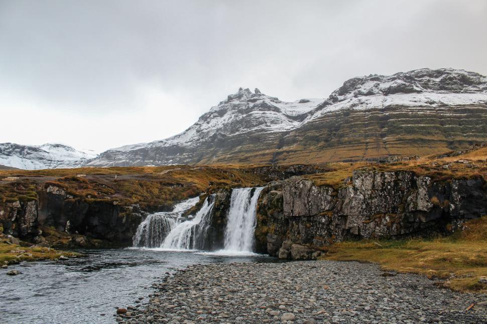 Free Image of A waterfall in a valley with snow covered mountains 
