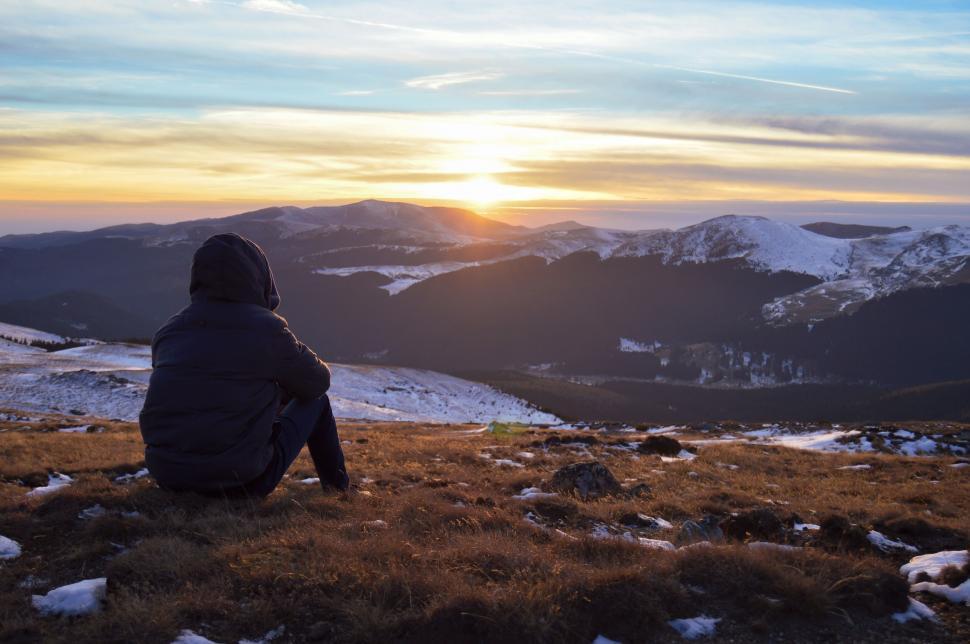 Free Image of A person sitting on a hill looking at the sun 
