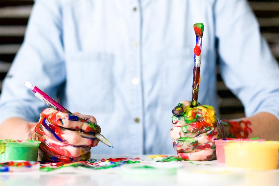 Free Image of A person holding paintbrush and paint on their hands 
