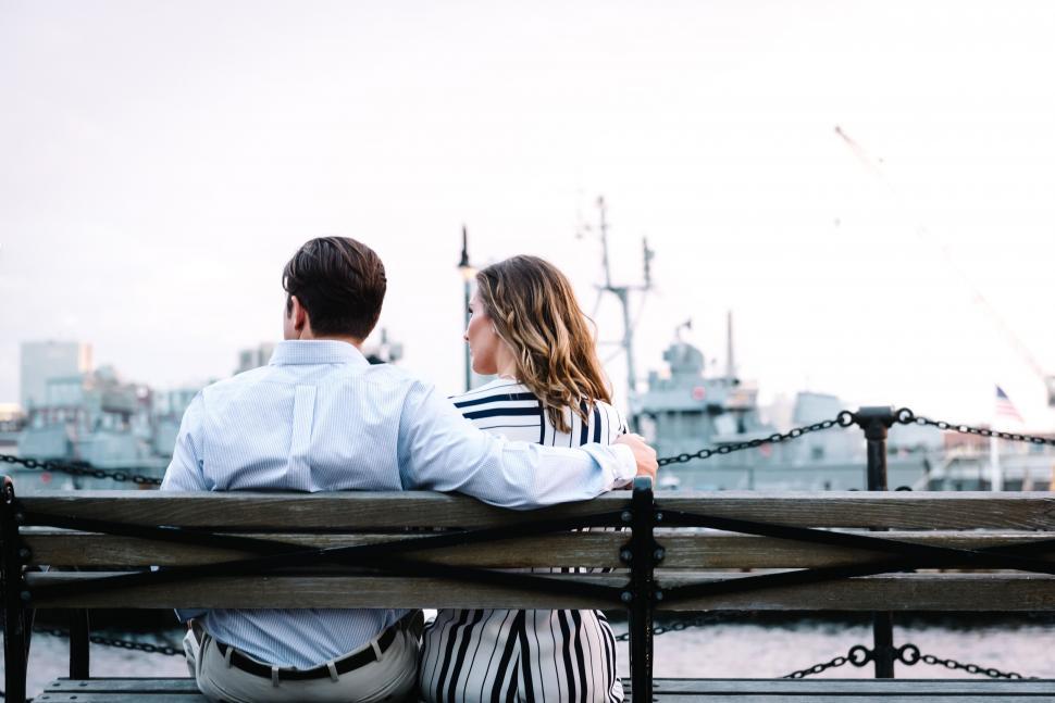 Free Image of A man and woman sitting on a bench looking at a ship 