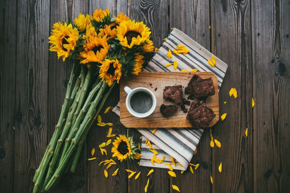 Free Image of A cup of coffee and brownies on a wood surface next to a bouquet of sunflowers 