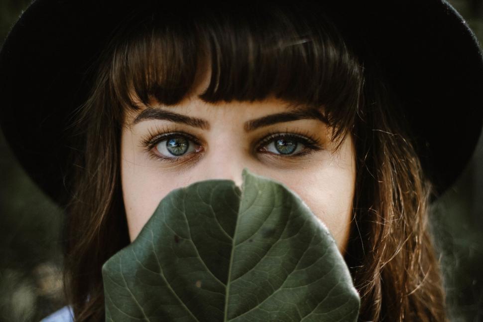 Free Image of A woman with blue eyes and bangs holding a leaf 