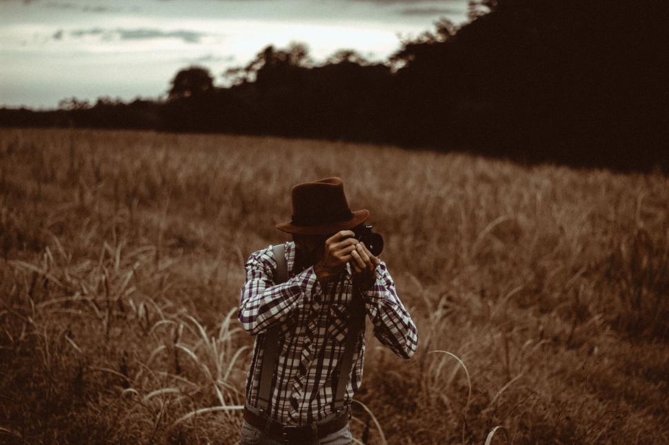 Free Image of A man in a hat taking a picture in a field 
