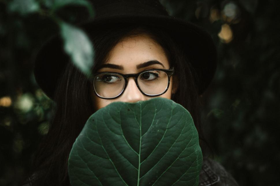Free Image of A woman with glasses and hat hiding behind a leaf 
