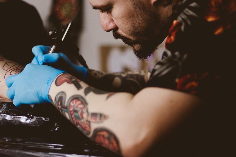Free Image of A man with blue gloves on his arm tattooing on his arm 