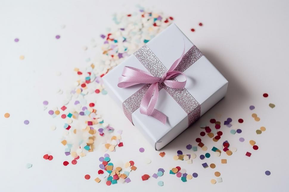 Free Image of A white box with a pink ribbon and a pink bow on top of a white surface with confetti 