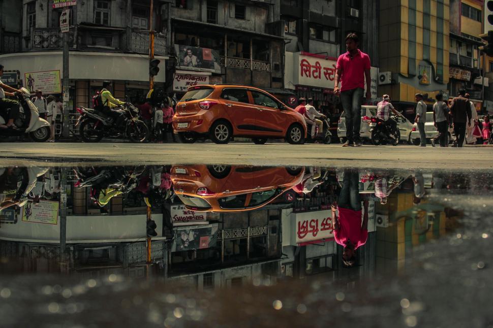 Free Image of A man standing on a street with a reflection of a car 