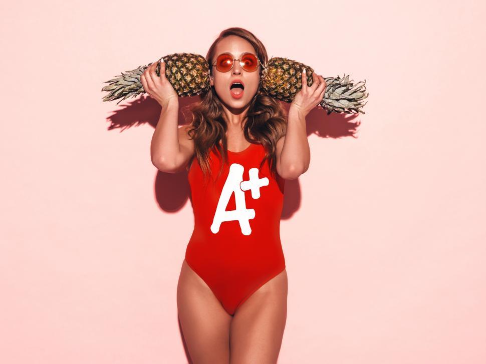 Free Image of A woman in a red swimsuit holding a pineapple over her head 