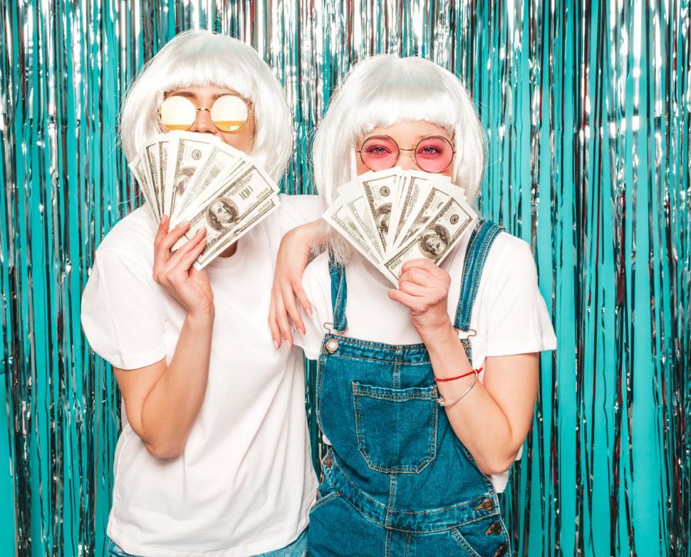 Free Image of Two women in white wigs holding money in front of their faces 