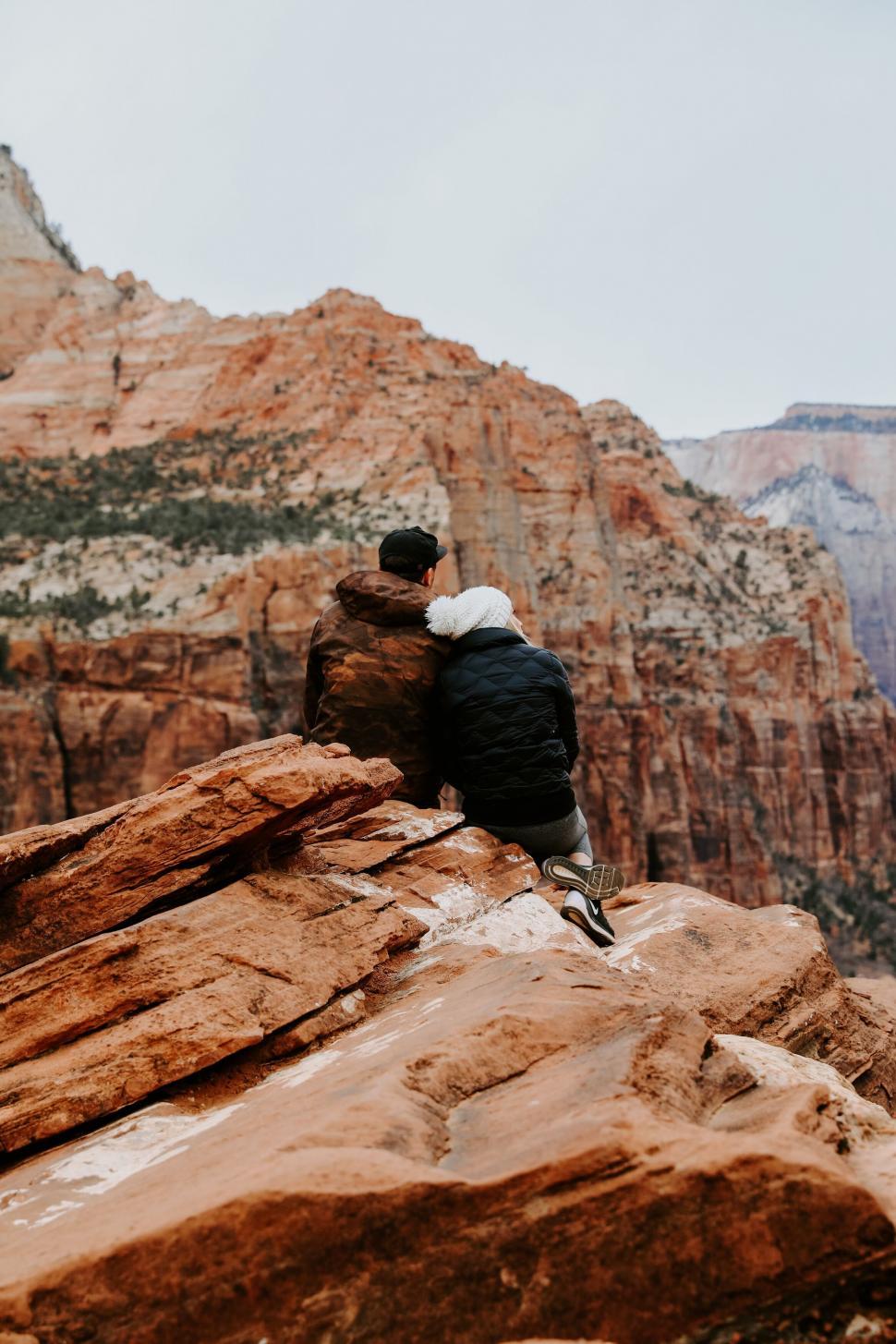 Free Image of A man and woman sitting on a rock looking at a canyon 