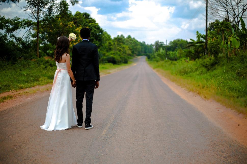 Free Image of A man and woman in wedding attire walking down a road 