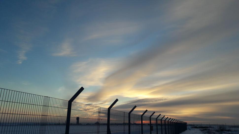 Free Image of A fence with a cloudy sky 