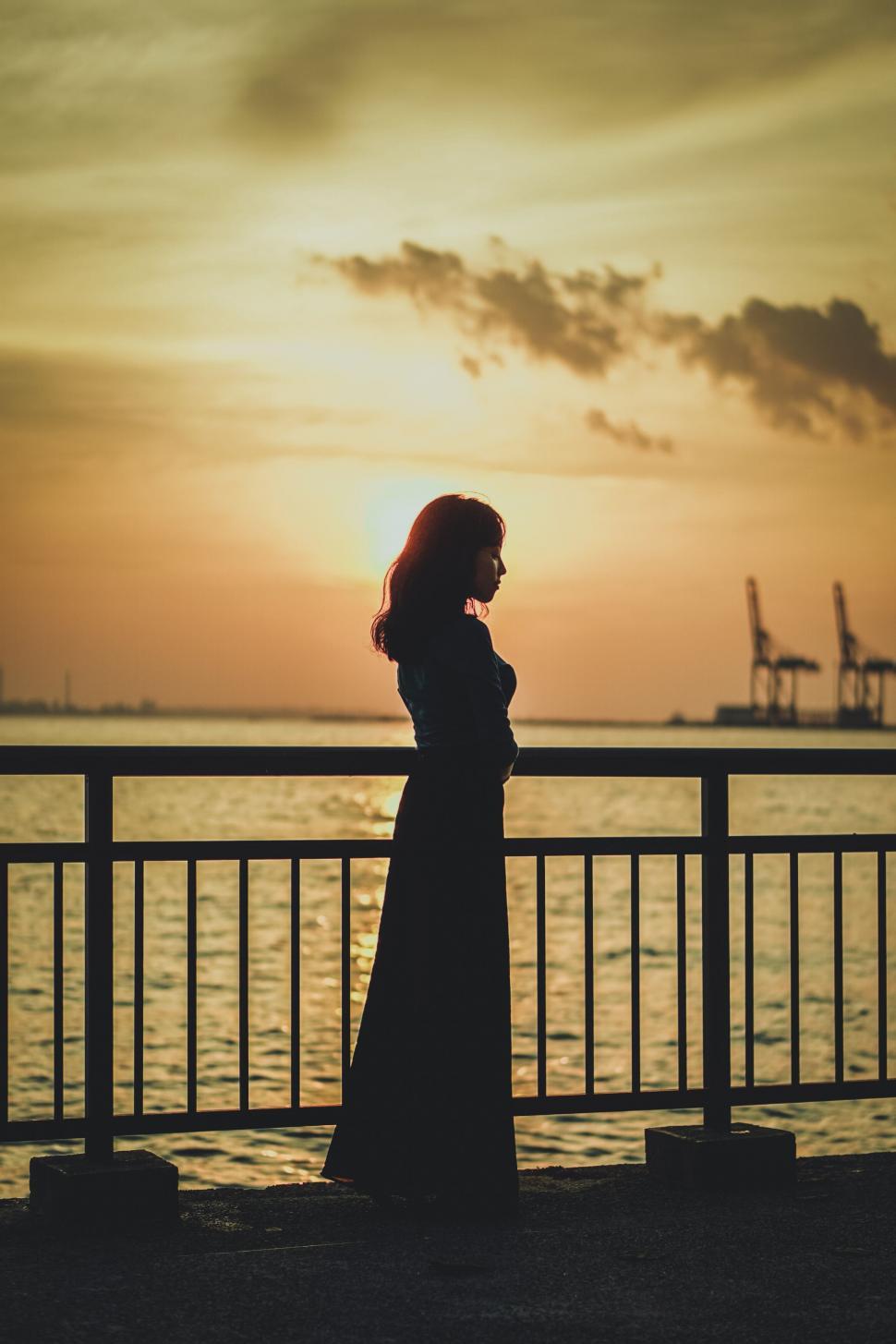 Free Image of A woman standing by a railing with a sunset in the background 