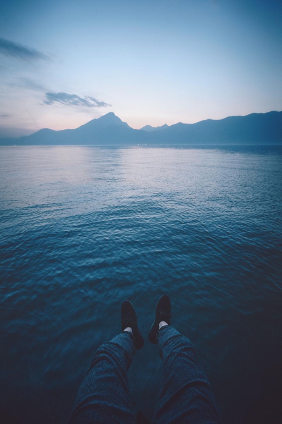 Free Image of A person s legs on a dock overlooking a body of water 