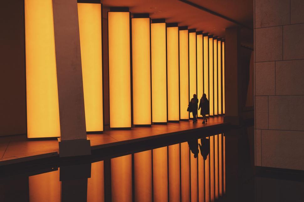 Free Image of Two people walking in a room with columns and lights 