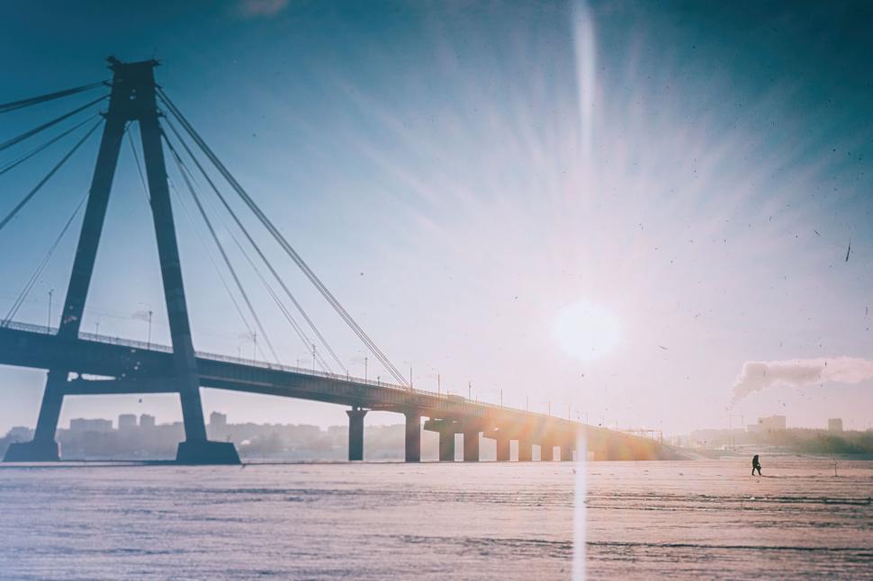 Free Image of A bridge over water with the sun shining through 