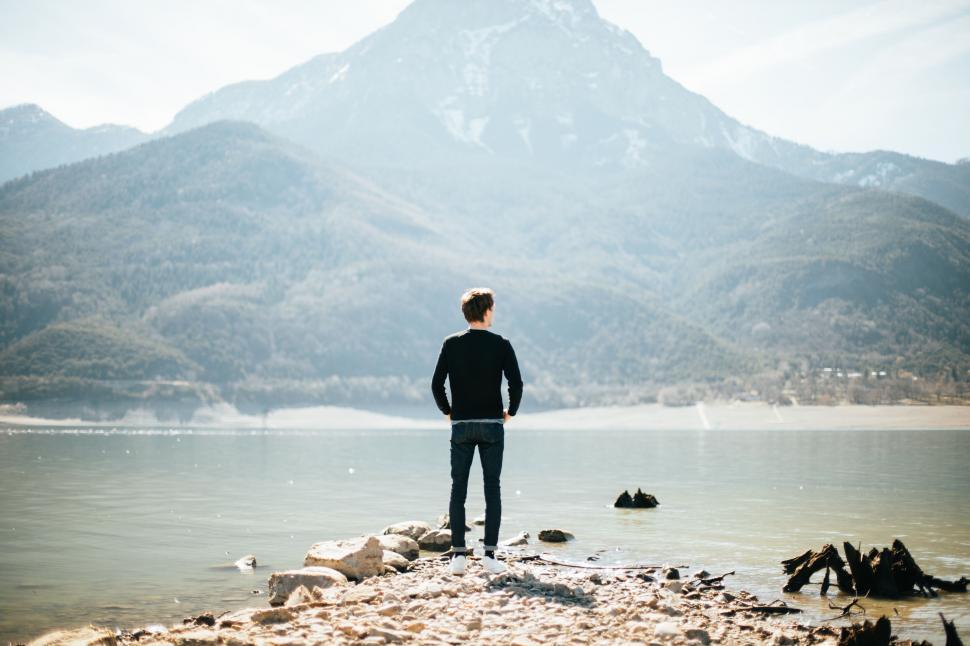 Free Image of A man standing on a rocky shore by a lake 