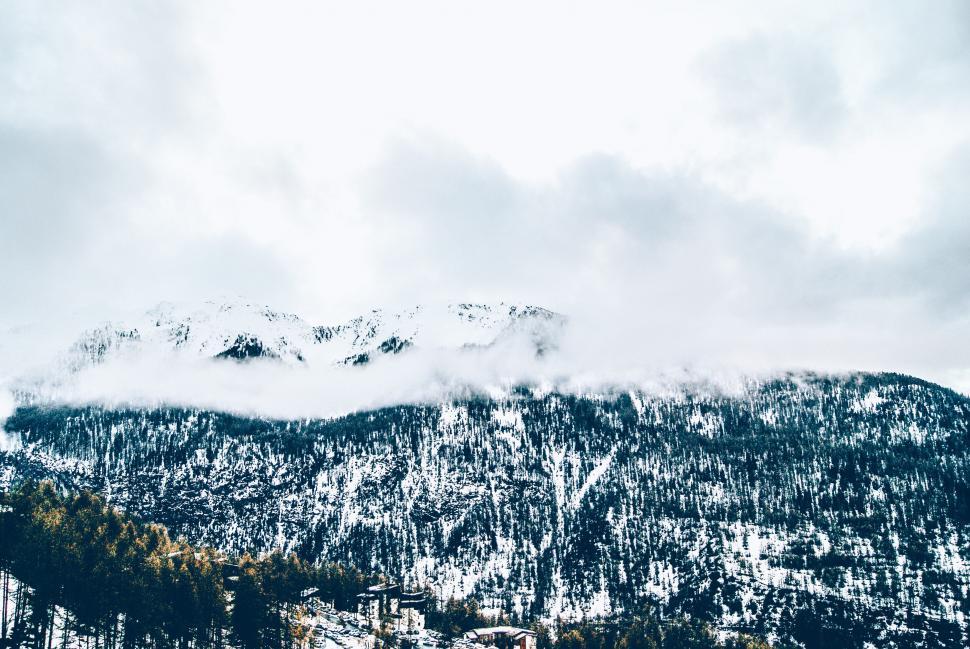 Free Image of A snowy mountain with trees and clouds 
