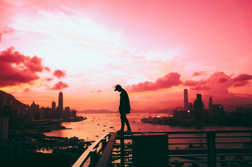 Free Image of A person standing on a railing overlooking a city 