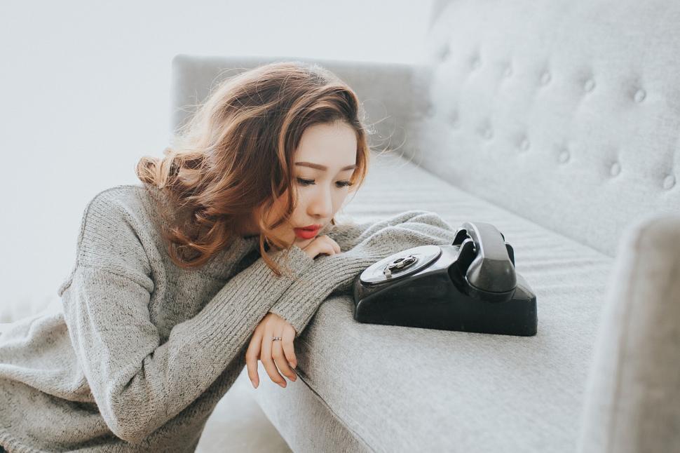 Free Image of A woman leaning on a couch with a telephone on it 