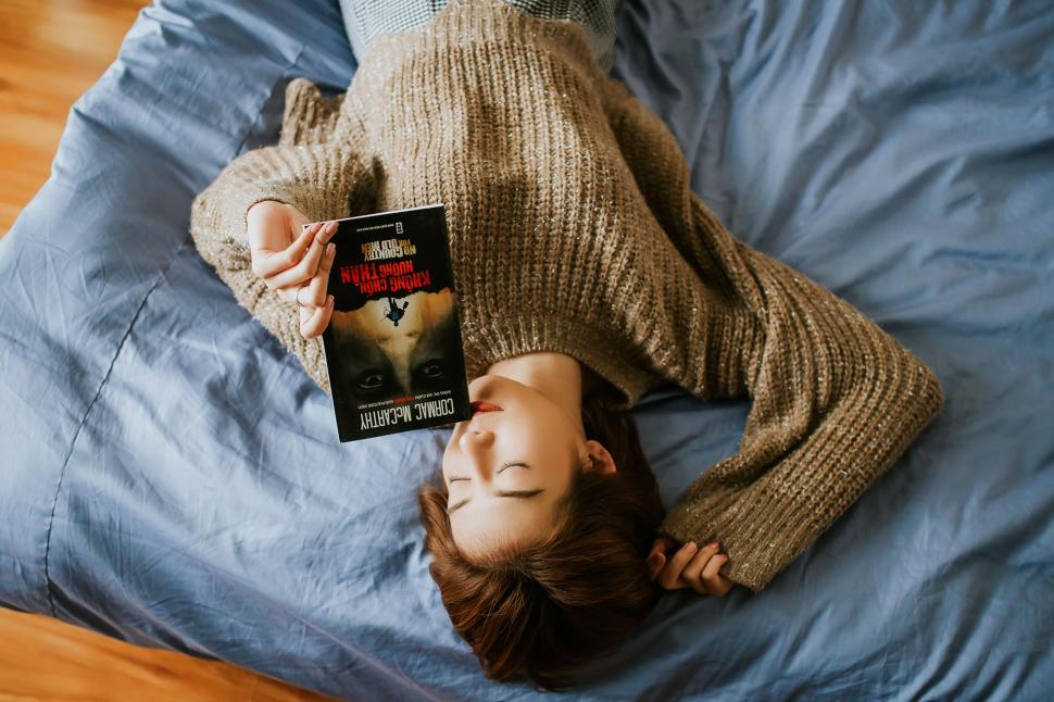 Free Image of A woman lying on a bed holding a book 