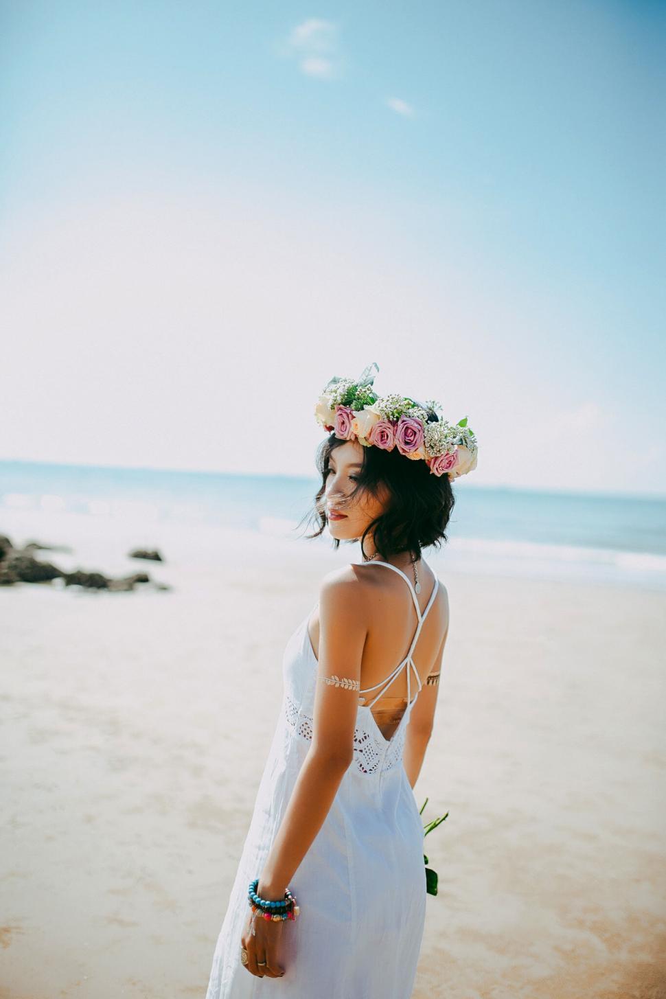 Free Image of A woman wearing a white dress and a flower crown on a beach 