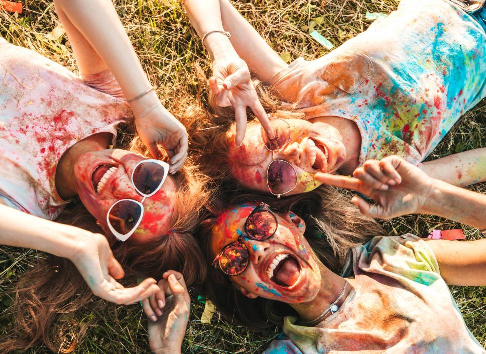 Free Image of A group of women lying in the grass with paint on their faces 