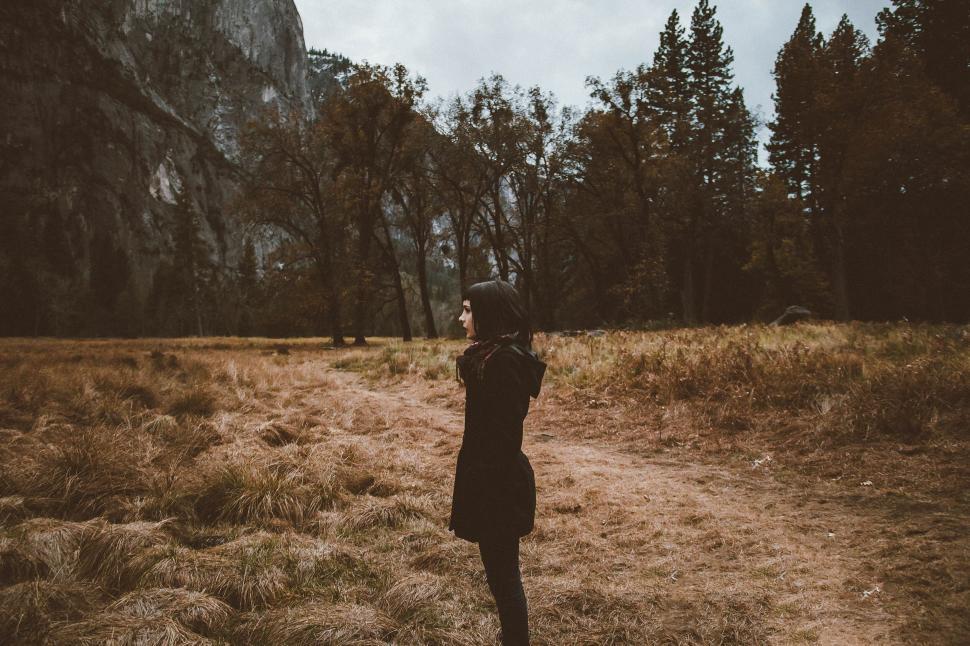 Free Image of A woman standing in a field with trees and mountains in the background 
