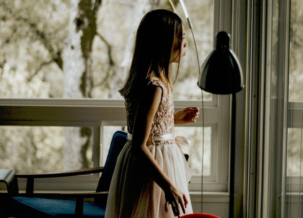 Free Image of A woman in a dress standing in front of a window 