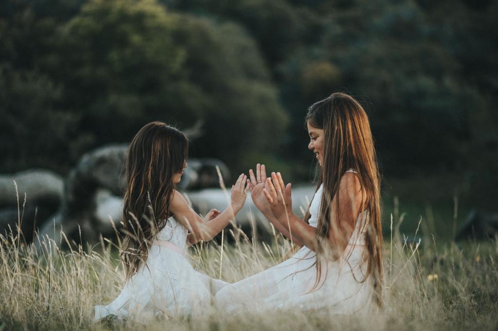 Free Image of Two girls in white dresses sitting in a field 