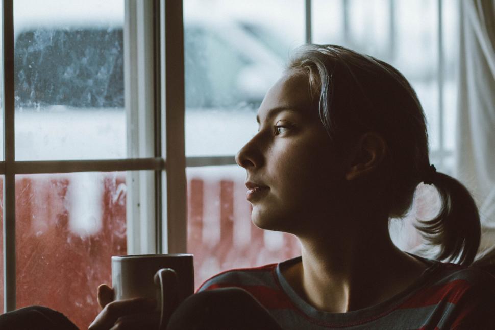Free Image of A woman holding a cup looking out a window 