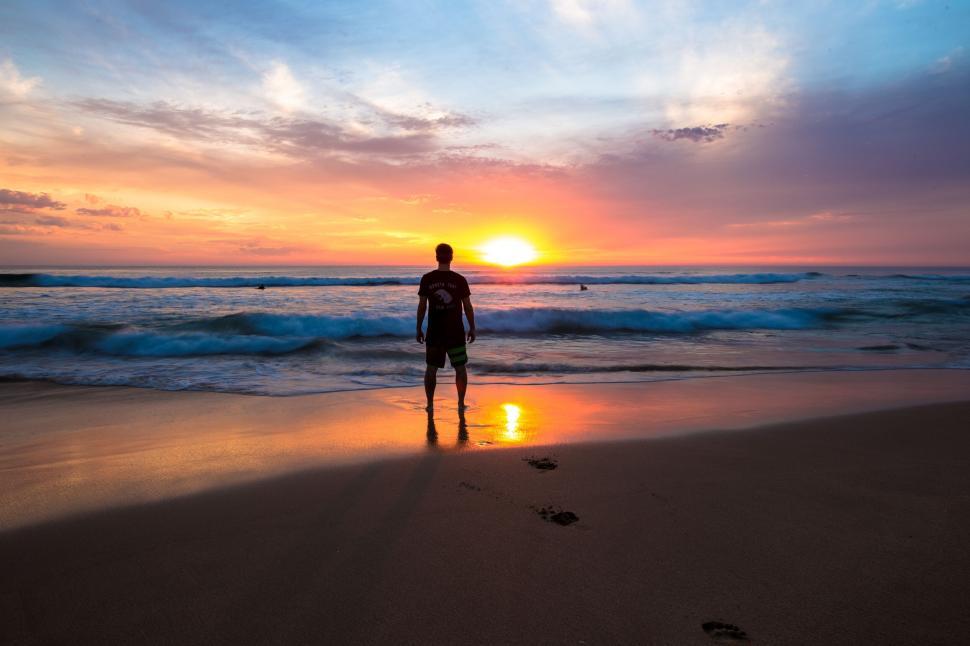 Free Image of A man standing on a beach at sunset 