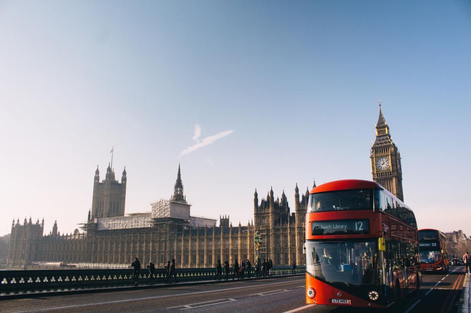 Free Image of A red double decker bus on a bridge with a clock tower in the background 
