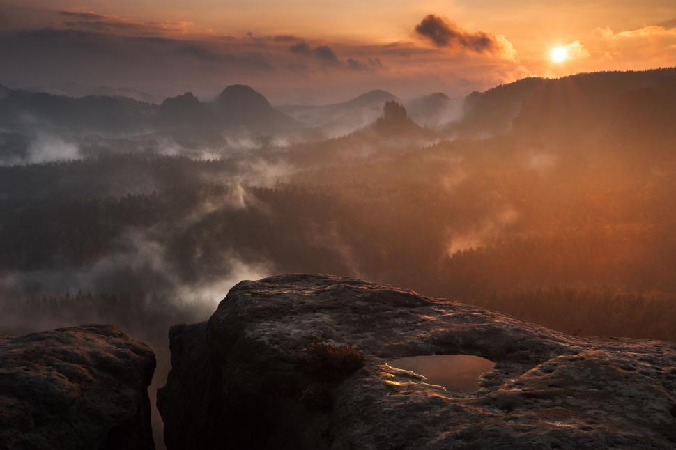 Free Image of A view of a valley with fog and mountains and a sunset 