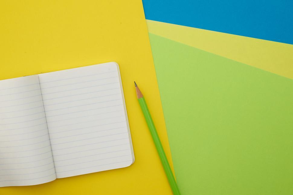 Free Image of A pencil and notebook on a yellow and blue background 