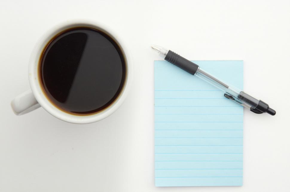 Free Image of A cup of coffee and a pen next to a notepad 
