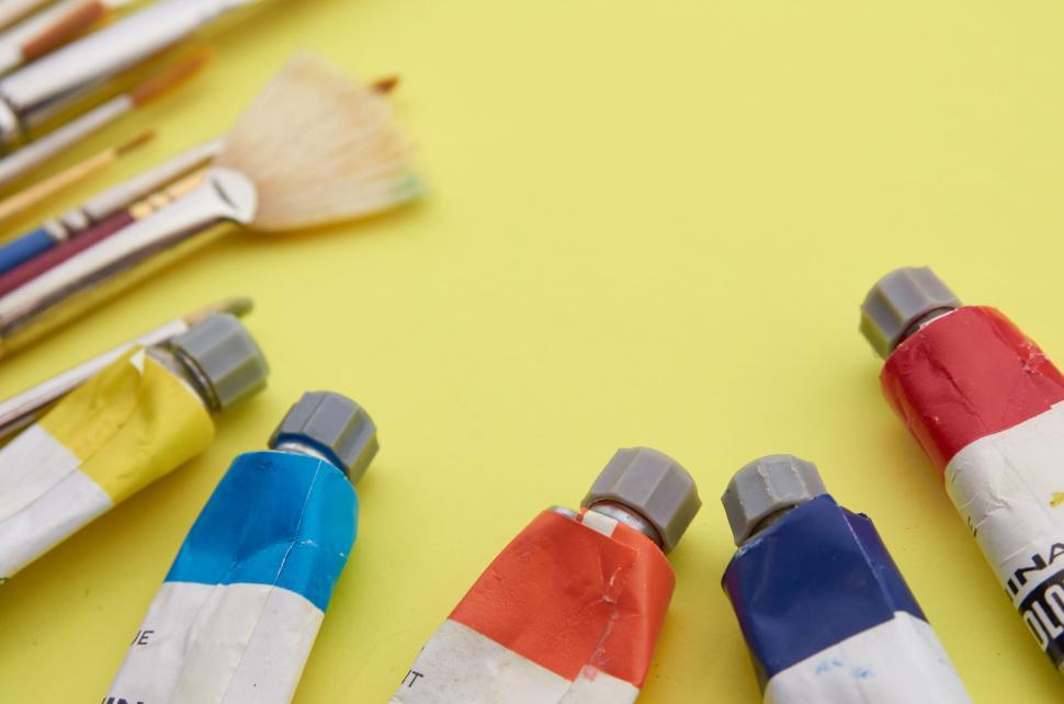 Free Image of Tubes of paint tubes and paintbrushes on a yellow surface 