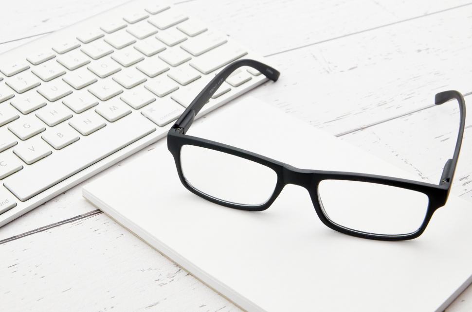 Free Image of A pair of glasses on a white notebook next to a keyboard 