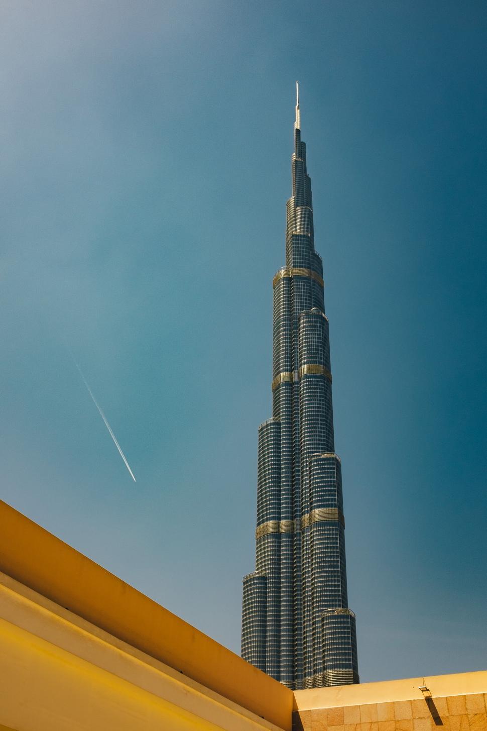 Free Image of A tall building with a jet in the sky with burj khalifa in the background 