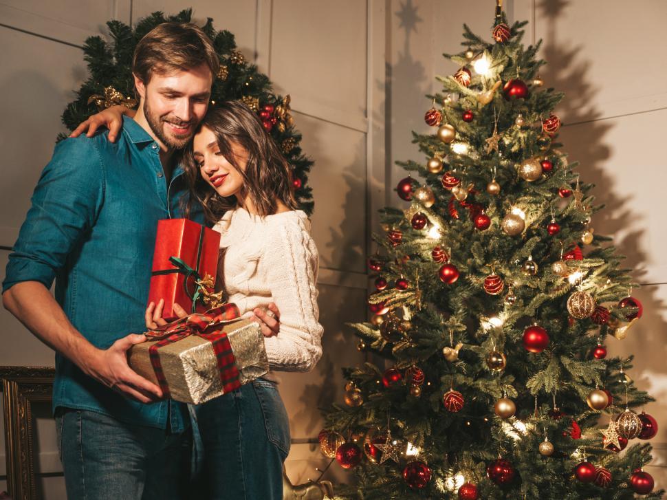 Free Image of A man and woman holding presents next to a christmas tree 