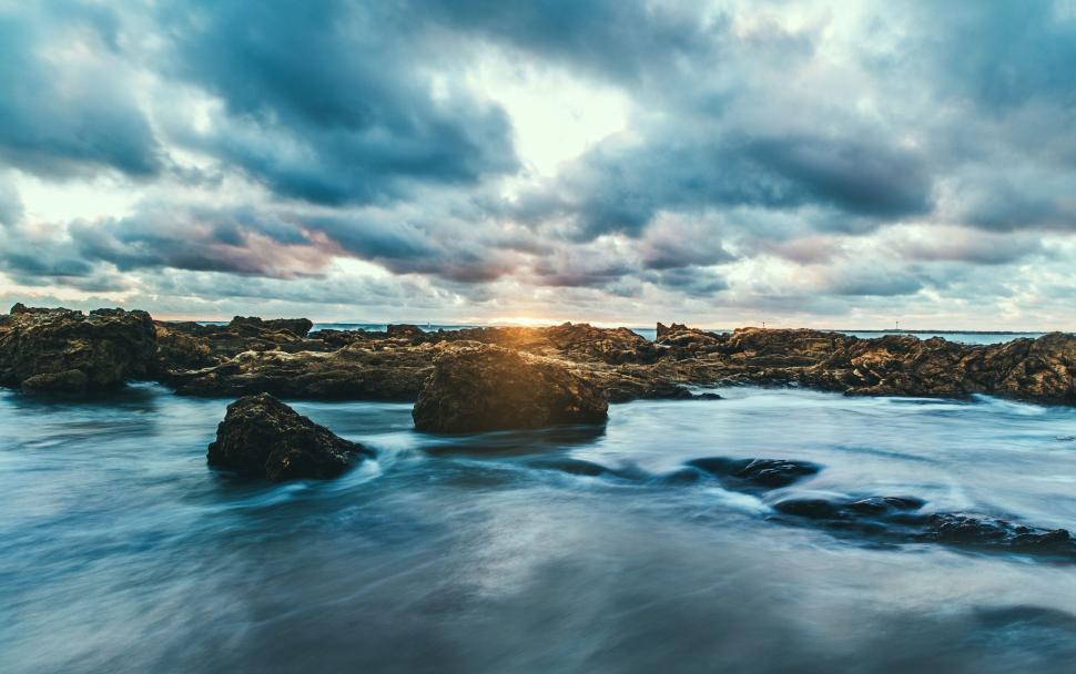 Free Image of A rocky beach with water and clouds 