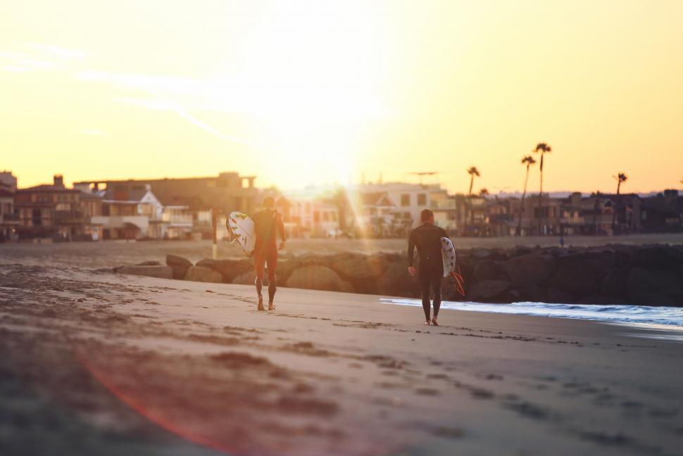 Free Image of Two people walking on a beach with surfboards 