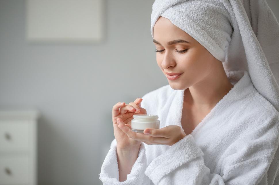 Free Image of A woman in a bathrobe applying cream 