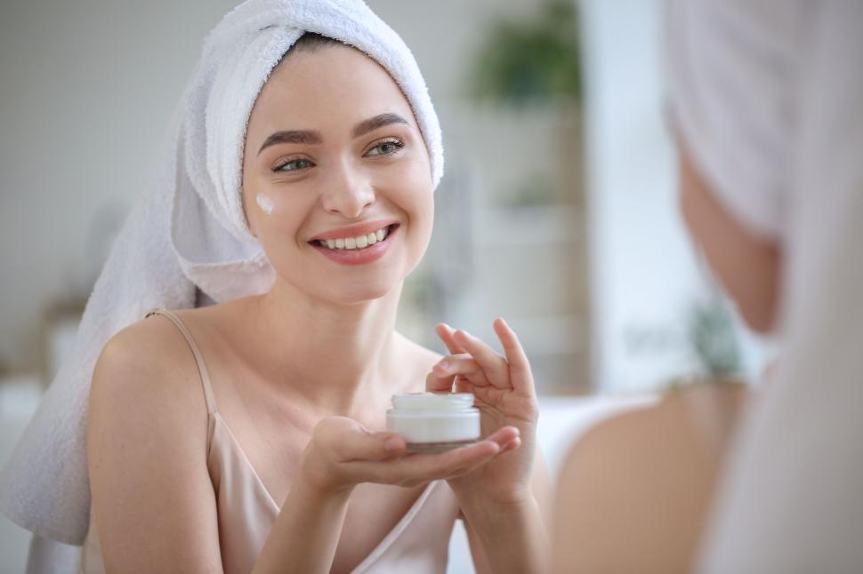 Free Image of A woman with a towel on her head holding a jar of cream 