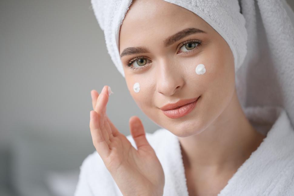 Free Image of A woman with a towel on her head applying cream on her face 