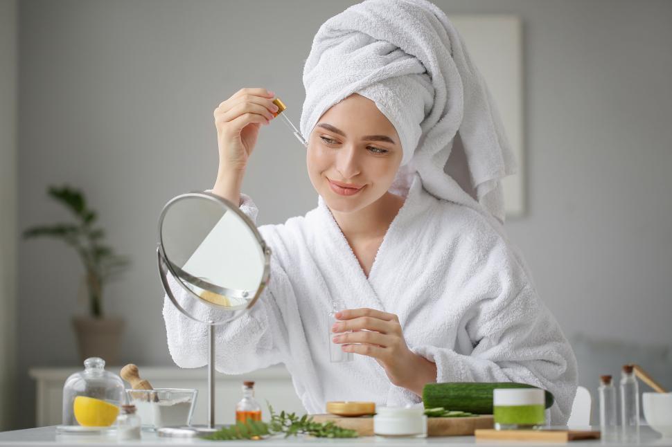 Free Image of A woman in a white robe and a towel on her head applying a dropper 