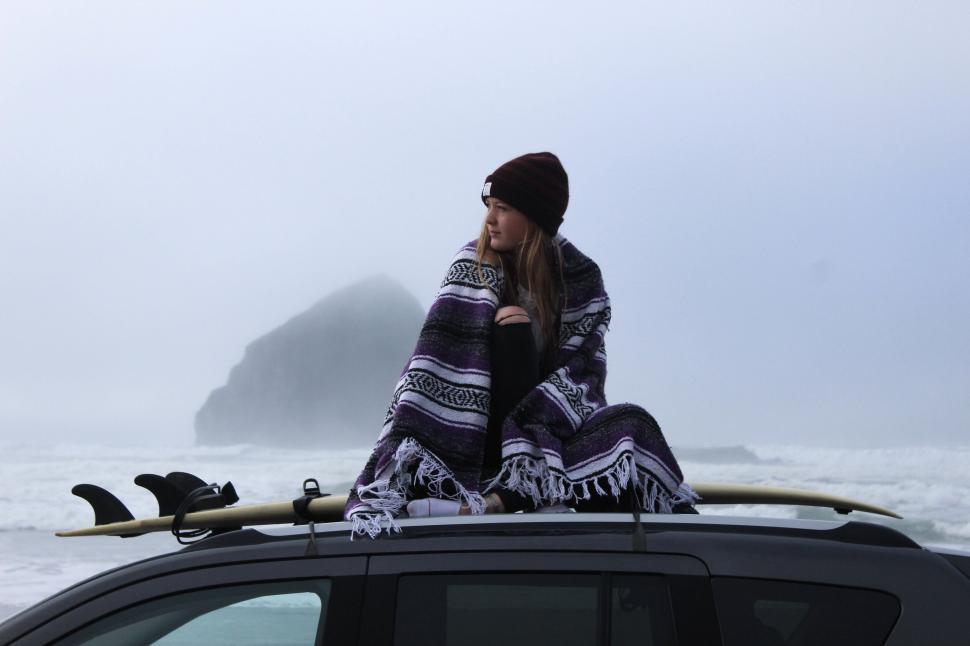 Free Image of A woman sitting on the roof of a car with a surfboard 