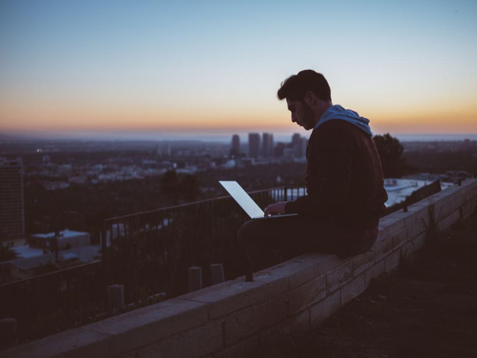 Free Image of A man sitting on a ledge with a laptop 