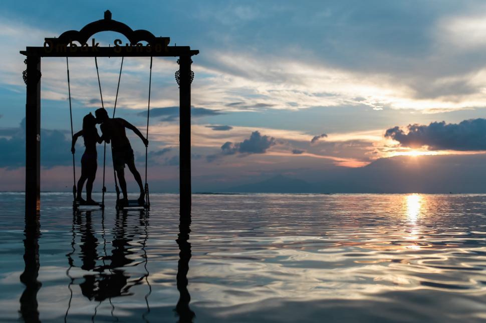 Free Image of A couple of people on a swing in the water 